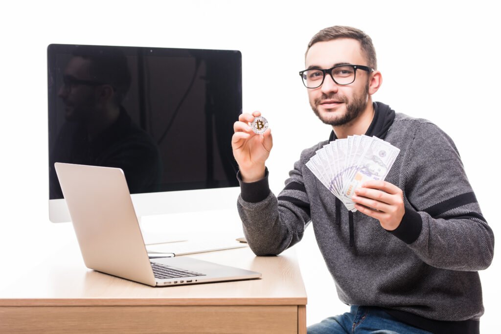 Handsome bearded man his working place with laptop pc monitor screen back with bitcoin dollars cash hands